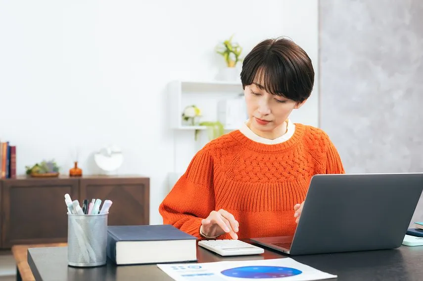 PCと計算機を使ってファクタリングについて調べている女性